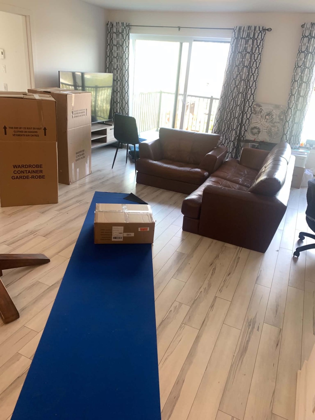 Living room with wardrobe cartons stacked and a blue runner across the floor before a move