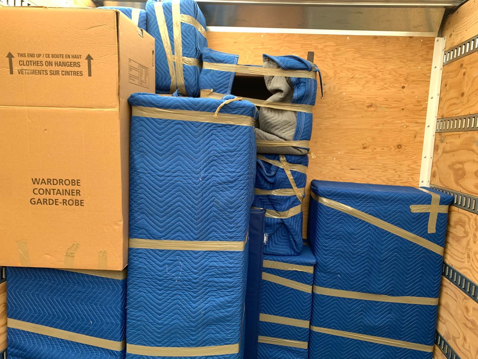 Blanket-wrapped furniture and wardrobe cartons stacked and strapped in tiers inside the truck